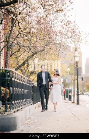 Couple élégant marchant sous les arbres magnolia en fleurs Banque D'Images