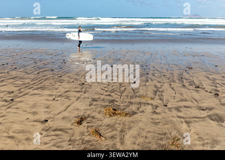 Un surfeur sur la plage de sable de 5 km de Playa de Famara dans l'île Canaries de Lanzarote, Espagne Banque D'Images