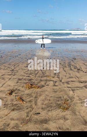 Un surfeur sur la plage de sable de 5 km de Playa de Famara dans l'île Canaries de Lanzarote, Espagne Banque D'Images