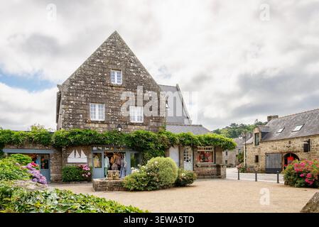 Maisons traditionnelles en pierre avec des toits d'ardoise et des façades fleuries dans le village historique de Locronan dans le Finistère Bretagne France montrant des magasins locaux, des hortensias et une atmosphère estivale sous la lumière douce du jour Banque D'Images