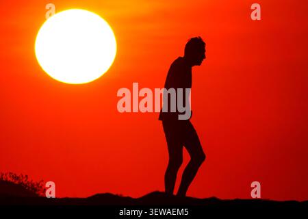 Île de Palms, États-Unis. 26 juin 2026. Un homme âgé marche devant le soleil levant qui silhouette son corps alors qu'il marche le long de la plage sur Wild Dunes, 26 juin 2026 à Isle of Palms, Caroline du Sud. Crédit : Richard Ellis/Richard Ellis/Alamy Live News Banque D'Images