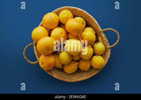 Vue d'en haut nature morte de citrons et de pamplemousses vibrants dans un panier tissé sur fond bleu Banque D'Images