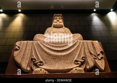 Grande statue de Bouddha en pierre assise avec des robes fluides et une expression contemplative vue de bas avec un éclairage dramatique au monastère de Chang Tai Chan Banque D'Images