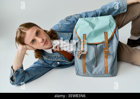 Charmant étudiant se détend sur le sol, présentant une tenue à la mode et un sac à dos tendance. Banque D'Images
