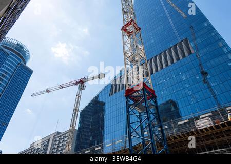Prise de vue en bas angle d'un chantier de construction animé avec un gratte-ciel en verre moderne et d'imposantes grues. Capture l'architecture contemporaine, le développement urbain Banque D'Images