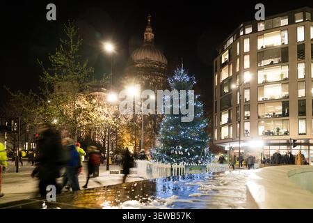 Les piétons passent devant une exposition « Christmas Tree Project » à Cheapside, Londres, tandis que la cathédrale de Saint Paul brille dans le décor festif. Banque D'Images