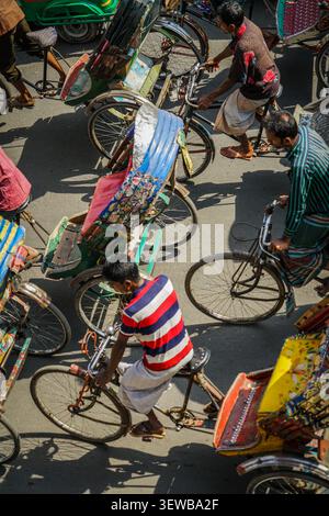 LIEU INCONNU, [VILLE] - 27 février 2017 : une vue en grand angle montre plusieurs tireurs de pousse-pousse et cyclistes sur une rue pavée, leurs ombres projetées longtemps Banque D'Images