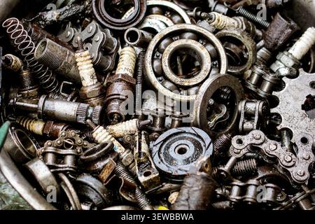 Une vue aérienne en gros plan montre une pile de divers composants de moteur de moto utilisés, y compris des roulements à billes argentés, des chaînes rouillées, des ressorts sales et des Banque D'Images