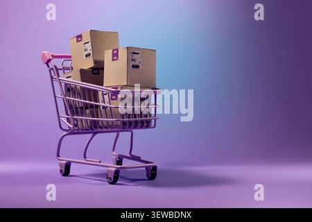 Chariot miniature rose rempli de plusieurs boîtes en carton étiquetées e-commerce. Idéal pour le commerce électronique, la vente au détail et les concepts liés au shopping. Banque D'Images