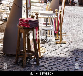 Les menus rouges sont empilés sur un tabouret en bois à côté de chaises blanches et de poteaux dorés dans un espace repas extérieur pavé Banque D'Images