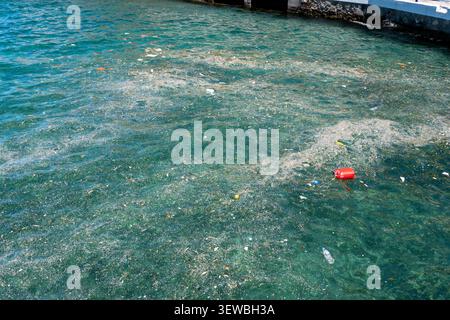 Une vue en grand angle de l'eau de l'océan fortement polluée par des bouteilles en plastique flottantes, des sacs, des bidons rouges, des microplastiques et de l'écume de déchets organiques accumulés Banque D'Images