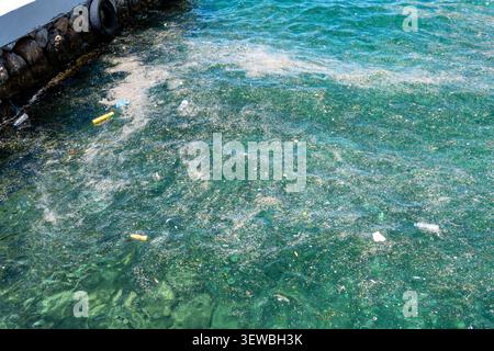 Une vue surélevée de l’eau de mer polluée par des bouteilles en plastique flottantes, des sacs, des pneus, des microplastiques et des déchets organiques accumulés près d’un ha de béton Banque D'Images