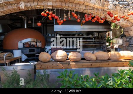 Cuisine méditerranéenne rustique du restaurant sous une arche en pierre avec un four à pizza au feu de bois, une rangée de grandes citrouilles sur un comptoir en bois, et des paquets Banque D'Images