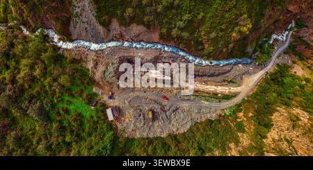 La vue aérienne capture un chantier de construction hydroélectrique dans une vallée de montagne accidentée. Une rivière turquoise dynamique coule le long du site, avec un U. Banque D'Images