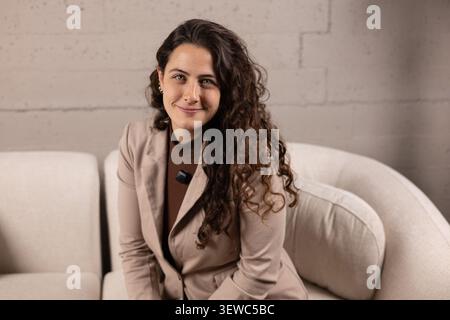 Jeune femme d'affaires avec les cheveux bouclés souriant tout en étant assis confortablement sur un canapé Banque D'Images