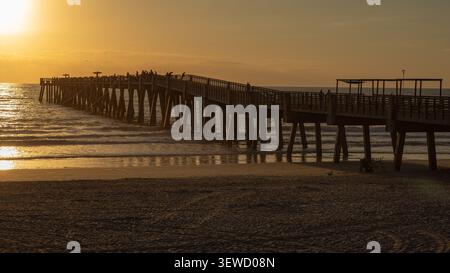 Belle lumière dorée au lever du soleil reflétant sur les colonnes de sable humide et de béton de la jetée de pêche de Jacksonville Beach. Banque D'Images