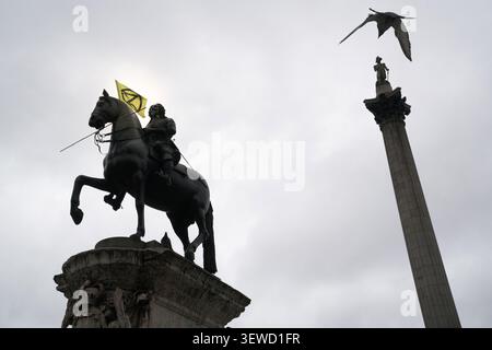 Les manifestants de la rébellion d'extinction arborent leur drapeau sur la statue du roi Charles Ier à Trafalgar Square à Londres pour exiger une action climatique urgente. Banque D'Images