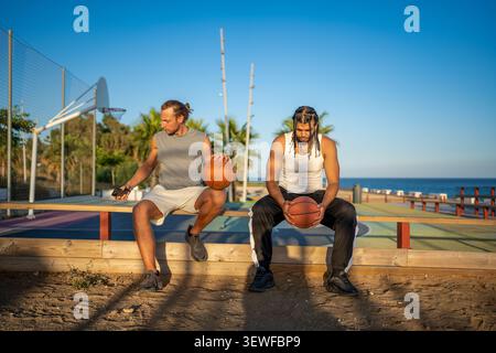 Joueurs de basket-ball masculins divers se relaxant sur le court de plage Banque D'Images
