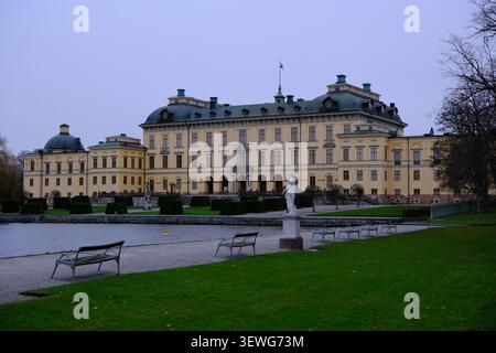 Stockholm, Suède-Nov.27th 2025 : Palais Drottningholm avec des bancs de parc, une statue et une pelouse au bord du lac sous un ciel couvert à Stockholm, Suède. Banque D'Images