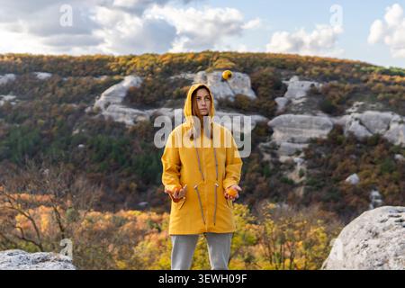 Jongler femme kaki sur le sommet de la montagne portant imperméable jaune pendant la randonnée d'automne Banque D'Images
