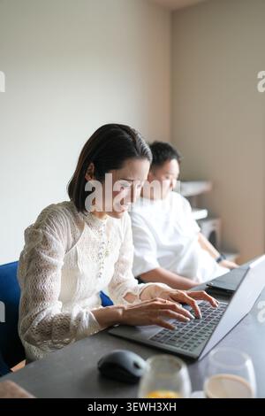 Une lumière douce illumine une femme concentrée tapant sur un ordinateur portable. Son expression calme suggère la concentration et le but. L'homme est assis tranquillement derrière elle, aussi e Banque D'Images