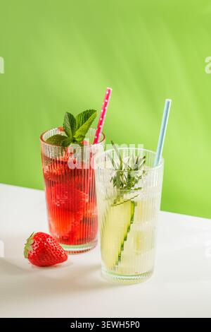 Deux boissons rafraîchissantes non alcoolisées avec fraise, concombre et herbes dans des verres sur fond vert vif. Boissons estivales saines avec espace copie Banque D'Images