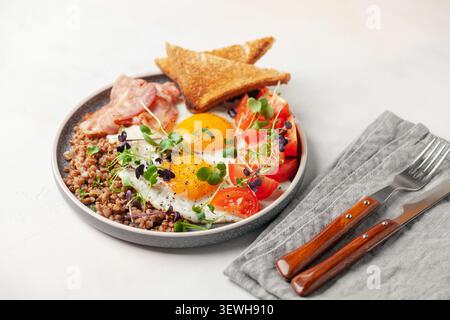 Petit déjeuner sain - œufs, pain grillé, sarrasin, bacon, haricots et tomates sur une assiette sur la table. Banque D'Images