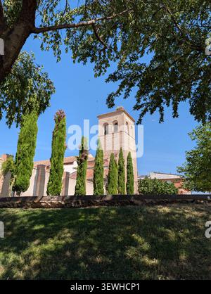 Une photographie en bas-angle, regardant à travers un cadre de branches d'arbres feuillus en surplomb, au vieux clocher en brique ensoleillé d'un coire de style espagnol Banque D'Images