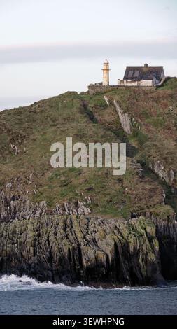 Un phare et une petite maison se dressent au sommet d'une falaise abrupte, herbeuse et rocheuse surplombant l'océan. Banque D'Images