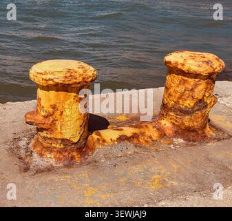 Bornes de port rouillées et poteaux d'amarrage sur une jetée en béton au bord de la mer en Grèce Banque D'Images