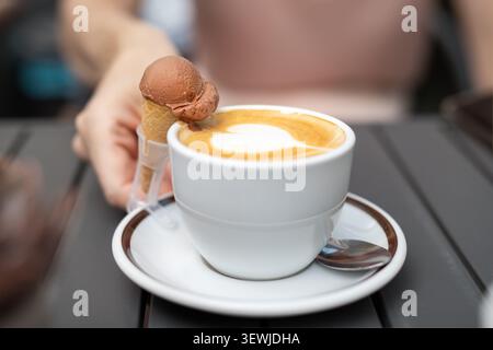 Un café au cœur de cappuccino crémeux latte art et un cornet de crème glacée au chocolat en miniature vous invitent. Pause café confortable mélange dessert, détente Banque D'Images