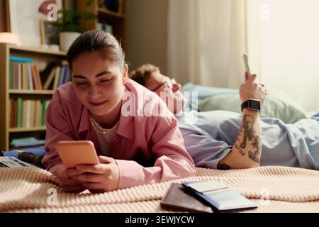 Jeune couple adulte utilisant des smartphones tout en préparant des vacances à la maison, en vérifiant les détails du voyage et les billets. Idéal pour la planification touristique, la réservation mobile, le marketing de style de vie de couple Banque D'Images
