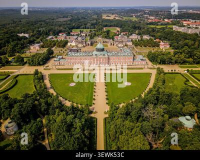 Une photo aérienne capture la grandeur du Nouveau Palais dans le parc de Sanssouci, Potsdam, avec sa façade rose distinctive et son dôme vert, entouré de meti Banque D'Images