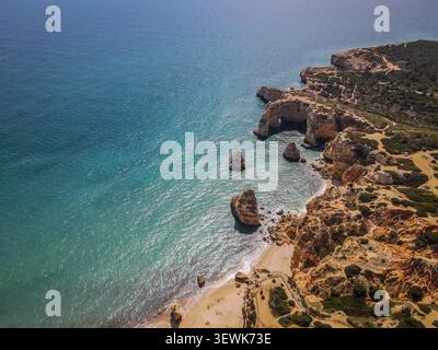Une vue aérienne montre l'océan Atlantique turquoise rencontrant la rive sablonneuse et les falaises de grès érodées de Praia da Marinha dans la région de Por en Algarve Banque D'Images