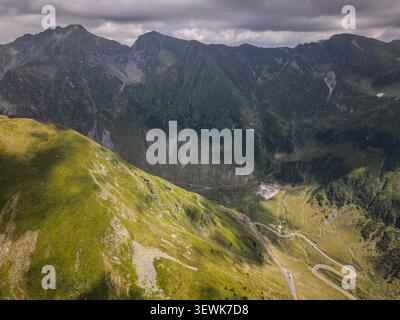 Une perspective aérienne capture la route sinueuse de montagne Transfagarasan alors qu'elle serpente à travers une vallée entourée de pics rocheux verts des Fagaras Banque D'Images