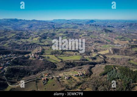Une vue aérienne grand angle met en valeur les collines ondulantes et les vallées de Saint-Marin avec les montagnes des Apennins au loin sous un ciel bleu clair. Banque D'Images