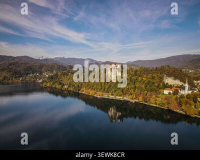 Une photo aérienne montre le lac de Bled avec le château de Bled sur une falaise et l'église paroissiale de Martin sur le rivage, soutenue par le feuillage d'automne et les Alpes juliennes. Banque D'Images