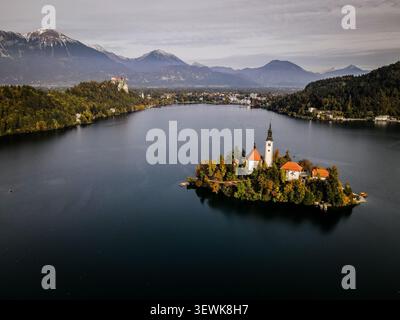 Une vue aérienne grand angle capture le lac de Bled avec l'île de Bled et son église Assomption of Mary Pilgrimage, entourée de feuillage d'automne, et Bled cas Banque D'Images