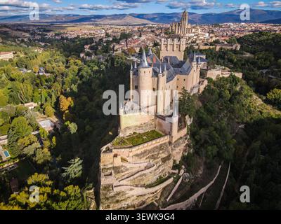 Une vue aérienne grand angle capture le Alcázar de la forteresse de Ségovie perché sur un éperon rocheux, entouré d'arbres verts, avec la ville de Ségovie et Banque D'Images