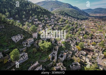 Une vue aérienne montre les maisons en pierre abandonnées et les structures de la ville fantôme de Kayaköy qui s'étendent sur une colline verdoyante. Ce village historique, autrefois un Banque D'Images