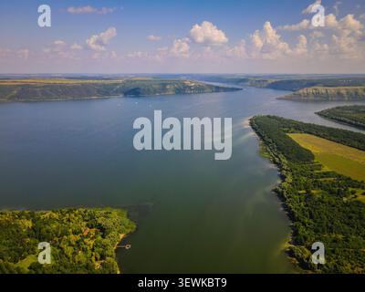 Une prise de vue aérienne capture le large fleuve Dniestr se courbant à travers des collines et des plaines vertes sous un ciel bleu avec des nuages blancs. Cette image est adaptée à Banque D'Images