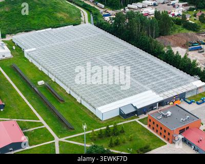 Rumbula, Lettonie - 24 juin 2026 : vue aérienne du complexe de serres Getlini EKO avec de grandes structures vitrées entourées de champs verdoyants et d'indu Banque D'Images