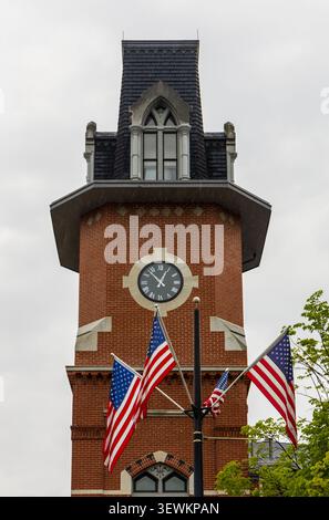 Tour de l'horloge du Richard et Nancy Donahue Family Academic Arts Center, à Lowell, Massachusetts avec drapeaux américains au premier plan. Banque D'Images