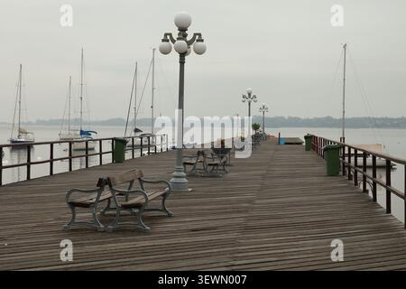 Jetée en bois avec lampadaires classiques, bancs et voiliers amarrés par une journée calme et nuageuse. Scène de front de mer photographiée à Colonia del Sacramento, U. Banque D'Images