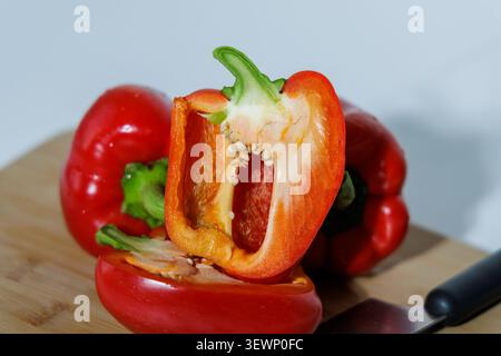 Trois gousses de paprika rouge juteux sur une planche de bois. L'un est coupé dans le sens de la longueur, exposant les graines et les membranes. Fond blanc, сlose-up, Banque D'Images