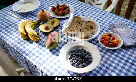 Étaler des fruits frais, du pain et du yaourt sur une nappe à carreaux bleus et blancs Banque D'Images