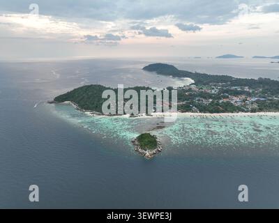 Vue aérienne de l'île de Koh Lipe entourée d'eaux turquoises, de récifs coralliens et d'une végétation luxuriante avec un petit îlot au premier plan à Tambon Ko Taruta Banque D'Images