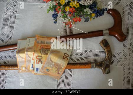 Une vue conceptuelle descendante de plusieurs billets de cinquante euros placés sur deux bâtons de marche vintage sur une nappe blanche, représentant des pensions seniors, ELD Banque D'Images