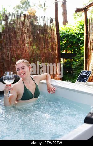 Expérience spa élégante avec une femme souriante dans un jacuzzi, profitant des loisirs, de l'auto-soin et de la détente. Banque D'Images
