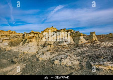 Vue panoramique des badlands de Bisti Wilderness montrant des formations de grès érodées et un terrain désertique sous le ciel bleu avec des nuages sinueux au Nouveau-Mexique Banque D'Images